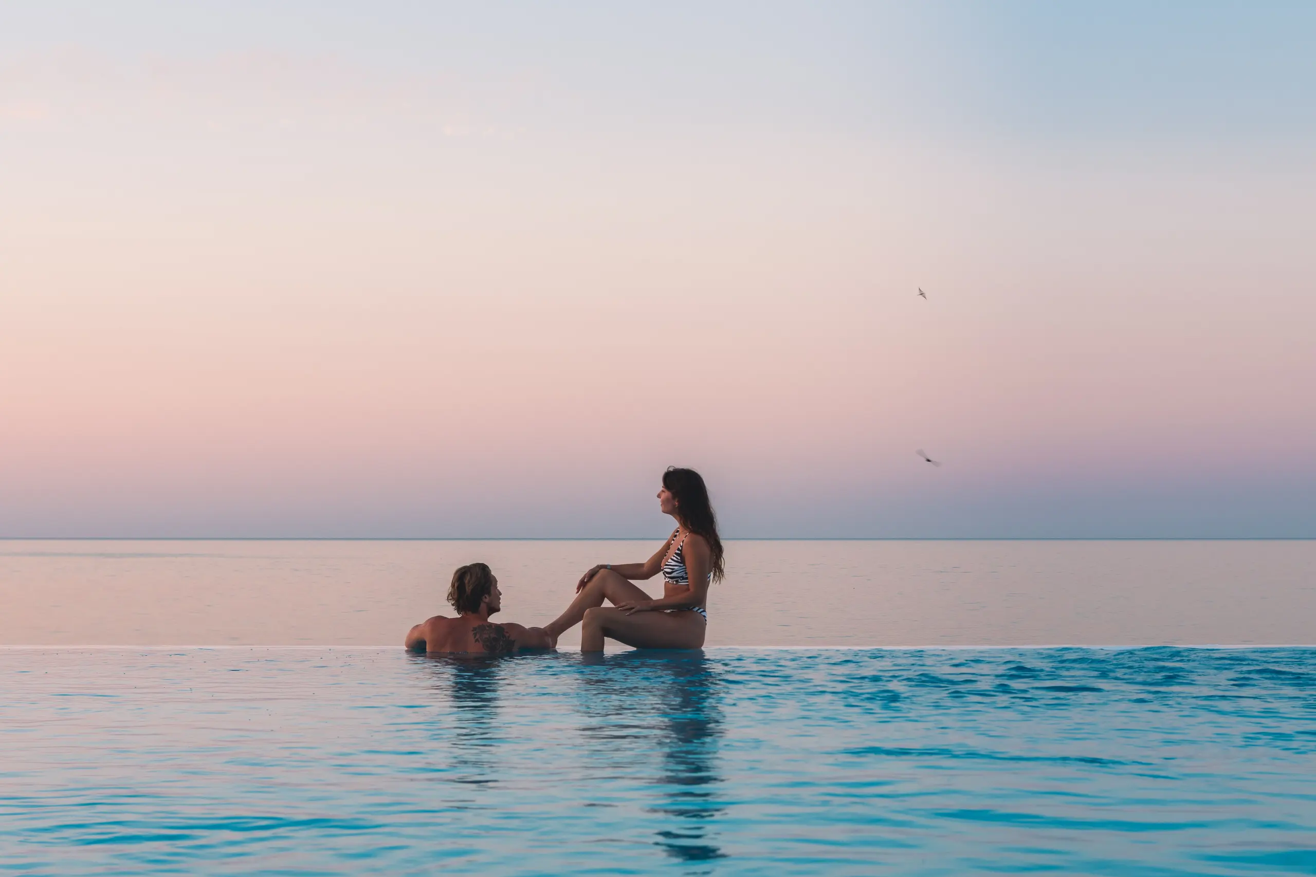 Arjan en Nikki bij het zwembad aan zee, tegen een roze lucht vlak na zonsondergang