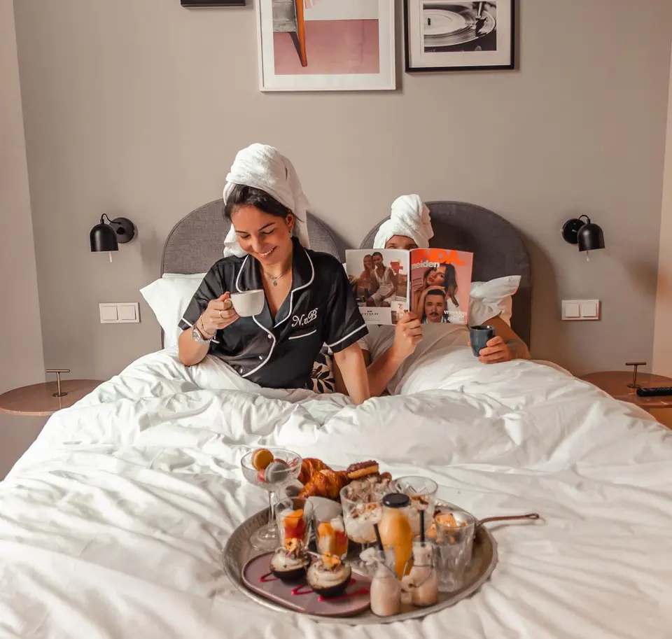 Arjan en Nikki in bed in een hotelkamer, handdoek om het haar, met een ontbijtblad tussen hen in